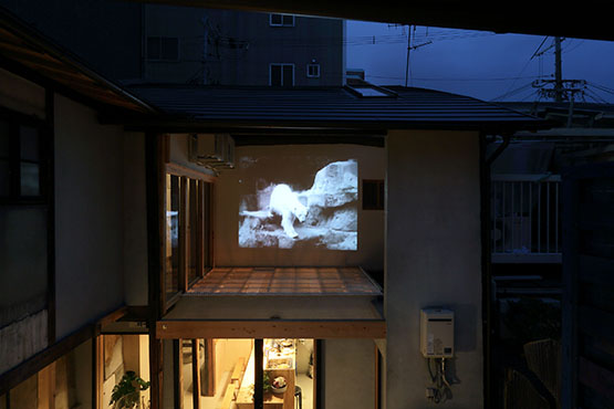 KYOTO ART HOSTEL kumagusukuにて開催された展覧会『光の洞窟』では東側のツインルームから中庭壁面に投影された映像を鑑賞することができた。 撮影:大西正一 画像提供:KYOTO ART HOSTEL kumagusuku