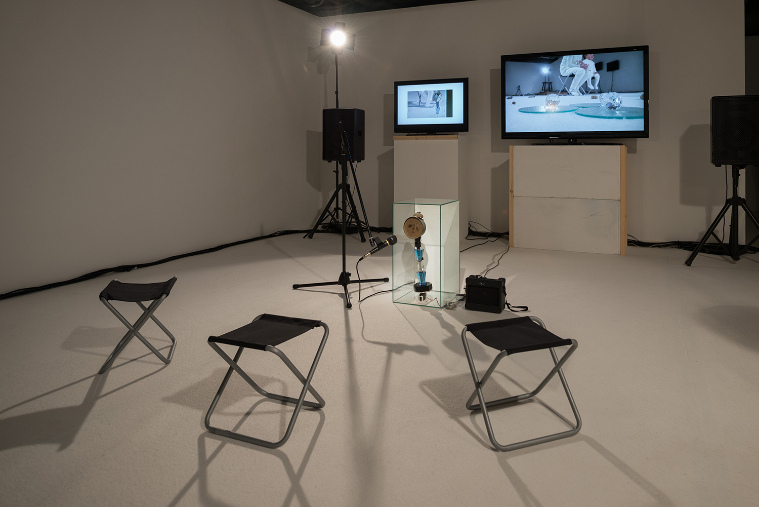 写真はARTZONEでの展示(オリジナル・ヴァージョン)。 “時計くん”の前に、撮影時に使用した“マイク”、“マイクスタンド”、“小さい椅子(3脚)”などが並んでいる。 撮影:表恒匡